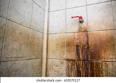 red cap water tap in dirty washroom with heavy stain of muddy black mold