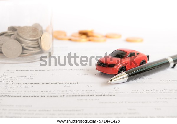 Red car, black ballpoint pen, glass jars with\
coins and gold coins on paper form, Blur with bright background,\
out of focus.