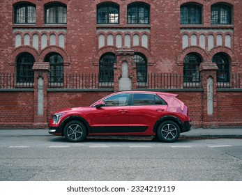 Red car, crossover type, parked in the street, side view on brick building symmetrical background - Shutterstock ID 2324219119