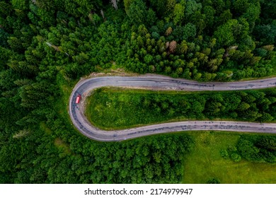 Red Car Driving Along The Mountain Asphalt Road. Road Through Beautiful Green Forest. Seen From The Air. Aerial Top View Landscape. Drone Photography. Mountain Serpentine