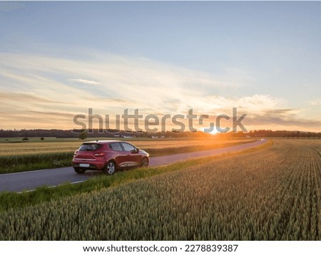 Red car driving down countryroad during sunset