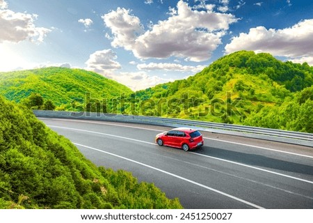 Red car driving on nature road between green mountains in summer. Nature landscape on highway for summer vacation travel. Mountain road view on beautiful nature trip in Europe. car drive on highway.