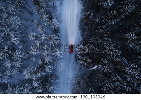 Red car driving on winter mountain road at night time. Beautiful aerial view with the trees covered in snow. Light in the dark.