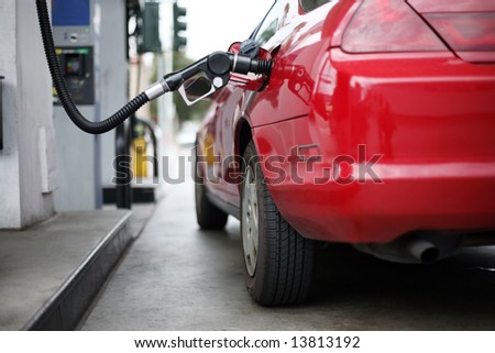 Red car at gas station being filled with fuel. Shallow DOF.