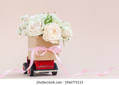 Red Car With A Gift Box Of Roses Flowers On The Roof On Pink Background. Happy Valentine's Day, Mother's Day, March 8, World Women's Day Holiday Card Concept, Flower Delivery.