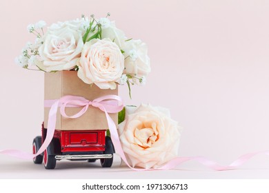 Red Car With A Gift Box Of Roses Flowers On The Roof On Pink Background. Happy Valentine's Day, Mother's Day, March 8, World Women's Day Holiday Card Concept, Flower Delivery.