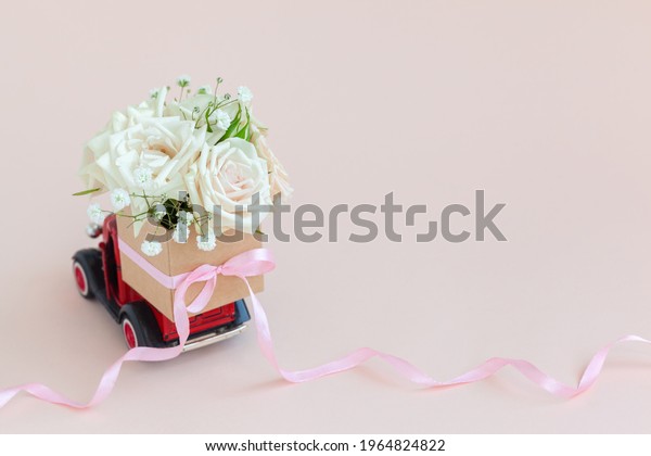 Red\
car with a gift box of roses flowers on the roof on pink\
background. Happy Valentine\'s Day, Mother\'s Day, March 8, World\
Women\'s Day holiday card concept, flower\
delivery.