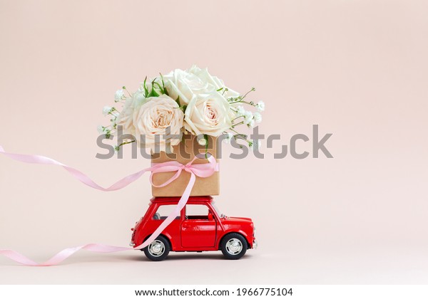 Red
car with a gift box of roses flowers on the roof on pink
background. Happy Valentine's Day, Mother's Day, March 8, World
Women's Day holiday card concept, flower
delivery.