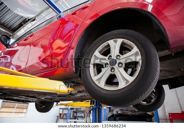 Red car lifted on hydraulic car lift in a\
workshop during routine\
service