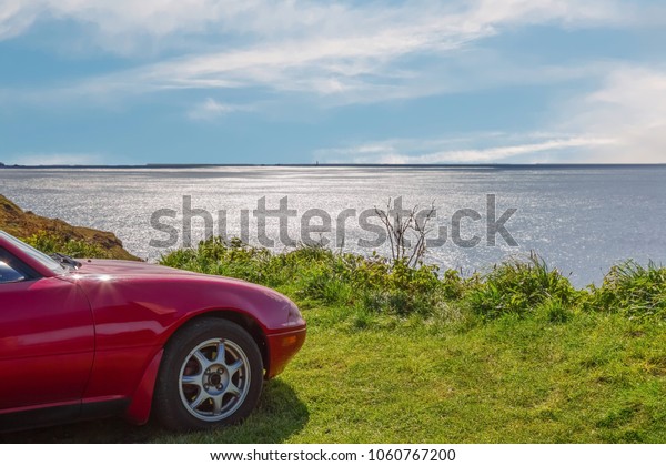 A red car on the\
cliffs with sea views