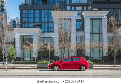 Red car on the empty urban street in a sunny day. Car parked in downtown of Vancouver Canada. Modern architecture view with car parked on a street. Nobody, street photo