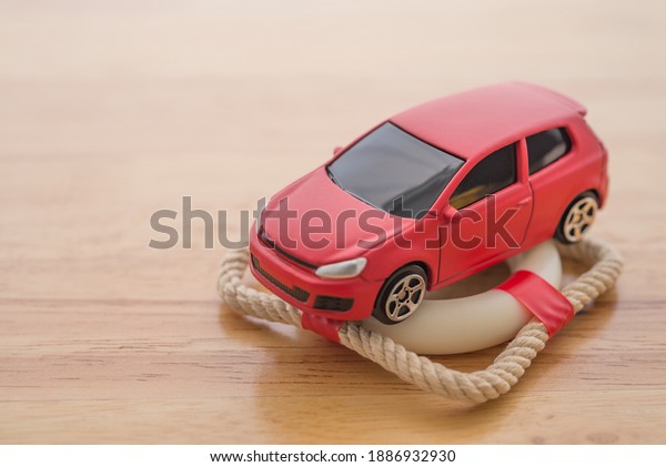 Red car on lifebuoy with wooden background with\
copy space. Auto insurance business concept. Check car insurance\
quote for get the best deal. Cover life, property damage, injury of\
third party.