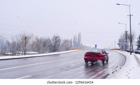 Red car on the road climbing a bridge, driving in difficult weather conditions in winter while snowing.