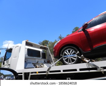 Red Car On A White Flat Bed Tow Truck With Blue Sky Background