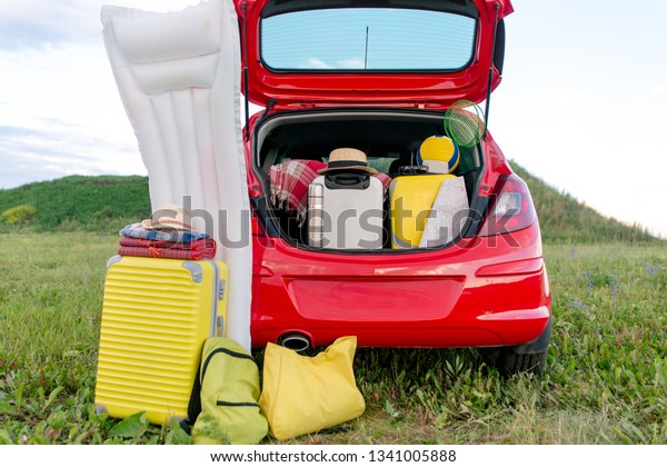 Red car with an open trunk with things for\
vacation and camping. Preparing to travel by car on a summer day in\
nature during the holiday\
season
