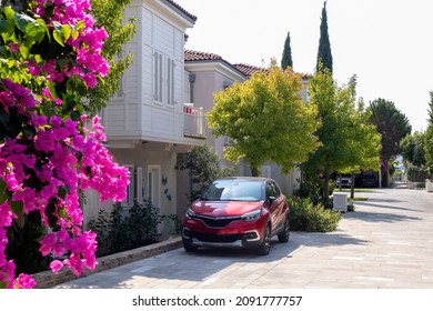 red car is parked near a private house, a lot of greenery and flowers