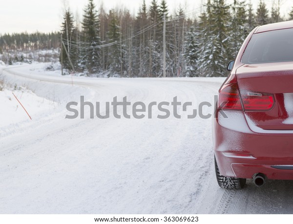 A red car is\
parked in the side of the road. The car is composed to the right\
side to emphasize the road next to it. Image taken during winter\
and the ground is covered with\
snow.