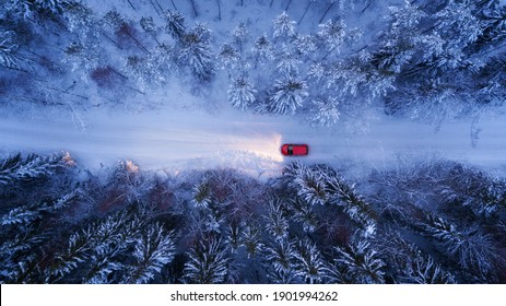 A red car rides along a winter road in the night forest. Snow on trees and roadsides, Aerial View.