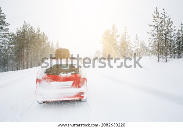 Red car with roof box on winter snow\
road.\
Snow winter forest with red car on the\
road.