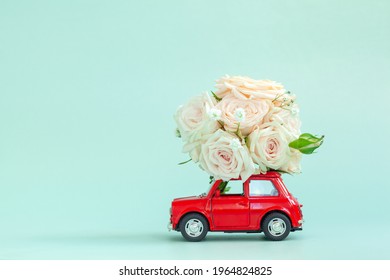 Red Car With A Roses Flowers On The Roof On Blue Background. Happy Valentine's Day, Mother's Day, March 8, World Women's Day Holiday Card Concept, Flower Delivery.