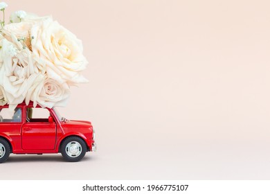 Red Car With A Roses Flowers On The Roof On Pink Background. Happy Valentine's Day, Mother's Day, March 8, World Women's Day Holiday Card Concept, Flower Delivery.