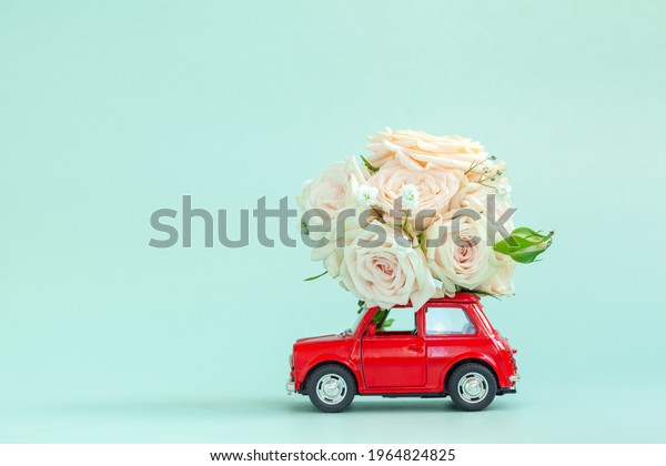 Red car with a roses\
flowers on the roof on blue background. Happy Valentine\'s Day,\
Mother\'s Day, March 8, World Women\'s Day holiday card concept,\
flower delivery.