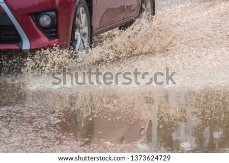 A red car speeding through the sewage road splashing yellow water splash