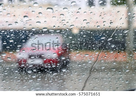 The red car through wet glass. Glass is covered with rain drops.
