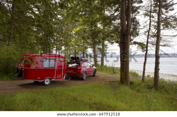 RED CAR WITH TINY CAMPER TRAILER CAMPING\
IN VANCOUVER ISLAND, BRITISH COLUMBIA, CANADA - May 10, 2017:\
Camping with tiny trailer, Vancouver\
Island