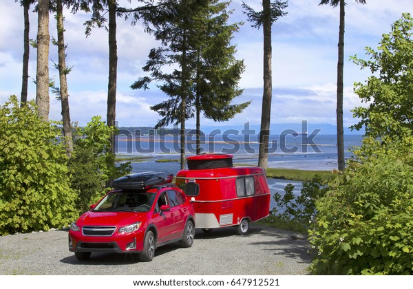 RED CAR WITH TINY CAMPER TRAILER CAMPING\
IN VANCOUVER ISLAND, BRITISH COLUMBIA, CANADA - May 10, 2017:\
Camping with tiny trailer, Vancouver\
Island