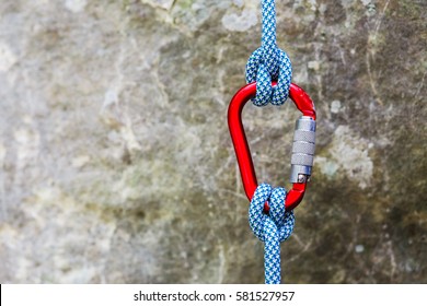 Red carabiner with climbing rope on rocky background. Climbing concept