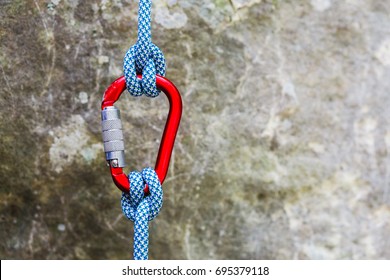 Red carabiner with climbing rope on rocky background. Climbing concept