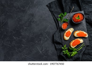 Red caviar in bowl and Sandwiches on stone board. Black background. Top view. Copy space
