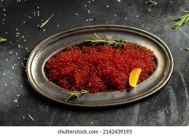 Red caviar in metal plate and a glass of champagne on a stone background. Gourmet food close up, appetizer, selective focus, place for text,