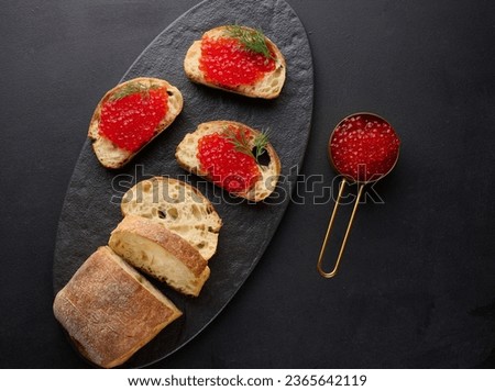 Red caviar on slices of white wheat bread on a black table, concept of luxury and gourmet cuisine