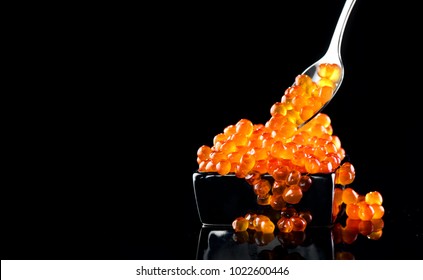 Red Caviar in a spoon. Caviar in bowl over black background. Close-up salmon caviar. Delicatessen. Gourmet food. Texture of caviar. Seafood.