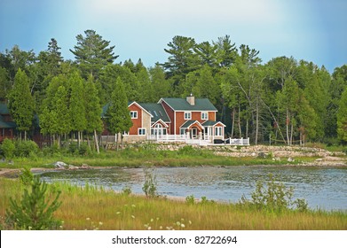A red cedar shake, two-story vacation home nestled in the pine trees on lakefront property in summer.