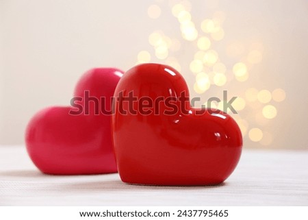 Red ceramic hearts on white table against blurred lights