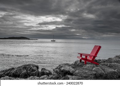 Red chair on ocean side rocks contrasts with the stormy black and white background. - Powered by Shutterstock