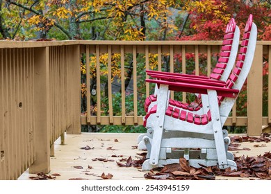 Red chairs with white framing on a wooden deck. Multicolored autumn leaves in bokeh background. Muted autumn colors on the trees frame deck chairs on a leaf covered deck. - Powered by Shutterstock