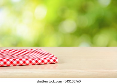 Red Checkered Cloth On Wood Table Top In Green Bokeh Abstract Background - Can Be Used For Display Or Montage Your Products