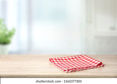 Red Checkered Folded Picnic Cloth On Wooden Table Empty Space Background.Towel Over The Plank Blurred Kitchen Background.