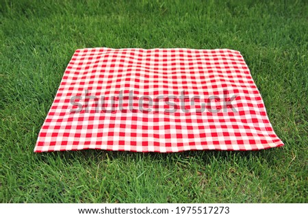 Red checkered gingham cloth on green grass. Picnic towel.Tabletop advertisement design. Food promotion display. Laying napkin.