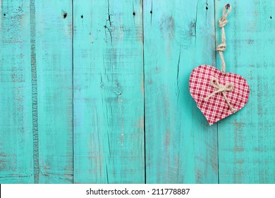Red checkered heart hanging from rope on antique teal blue wood fence