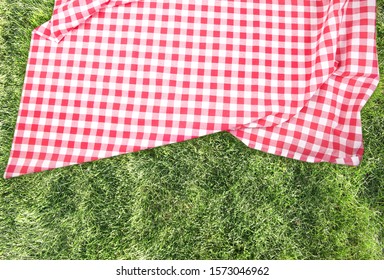Red checkered picnic cloth on green grass background top view.