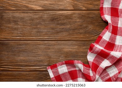 Red checkered tablecloth on wooden table, top view. Space for text