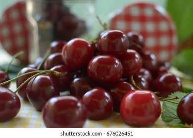red cherries with stems and leaf on yellow white dicey tablecloth jars and red white caps