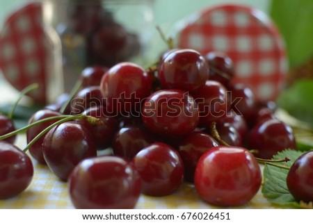 red cherries with stems and leaf on yellow white dicey tablecloth jars and red white caps