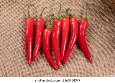 Red Chili Peppers 7 In A Row On Brown Burlap Texture Background. Bright Red Ripe Spicy Southwest Peppers For Drying, Cooking And Seasoning Food And Recipes