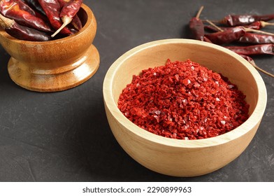 Red Chilli pepper seedless flakes in wooden bowl on black table. Organic red spicy korean. ingredients in Korea known as Gochugaru. used for kimchi, spicy fermented condiment in Korean food